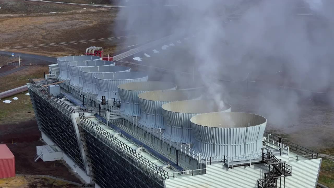 A row of cooling towers venting steam on an industrial power site, seen from the air